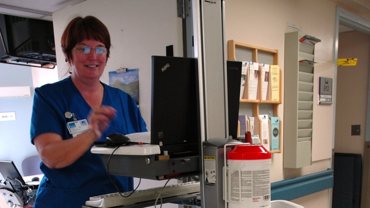 A nurse at a rolling computer cart in a hospital corridor