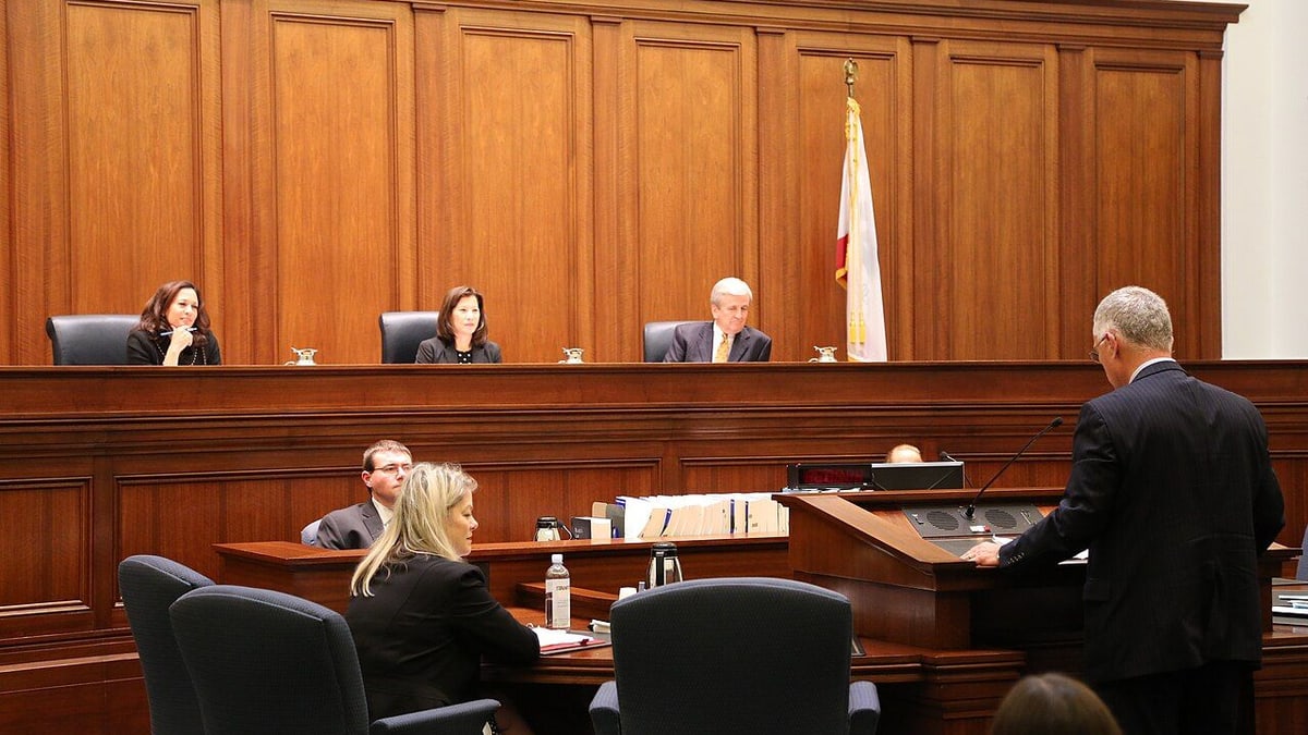 A speaker at a lectern addresses three justices in a wood-paneled California courtroom