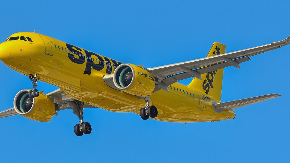 A yellow Spirit Airlines Airbus A320neo jet with its landing gear down against a clear blue sky