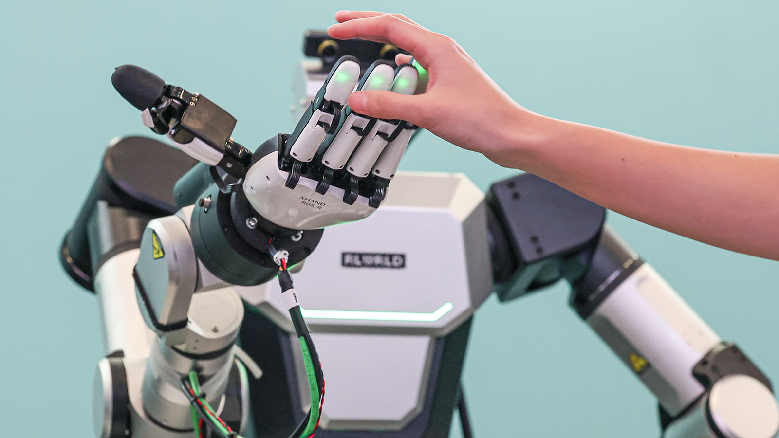 Humanoid robot hand with glowing green fingertips meeting a human hand at Humanoids Summit Seoul COEX demo