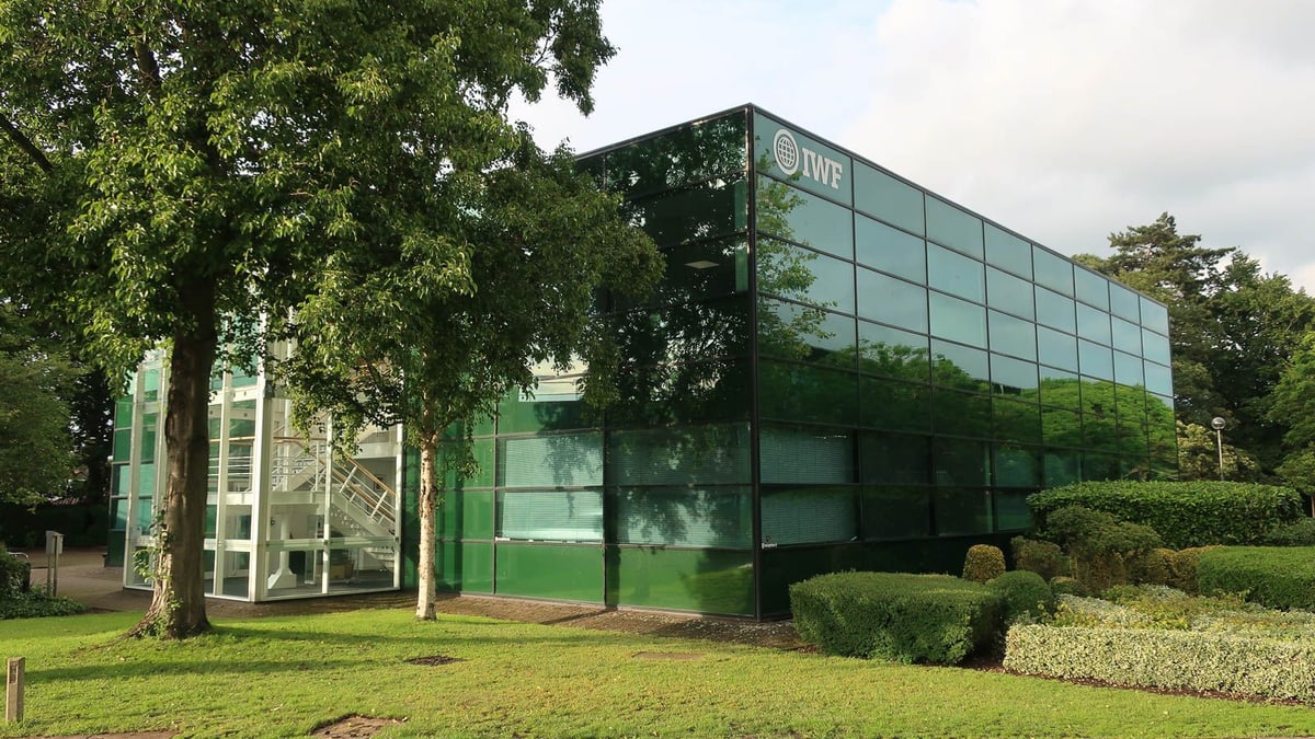 The Internet Watch Foundation's glass office building in Histon, near Cambridge, England, with the IWF logo near the roofline and trees in front