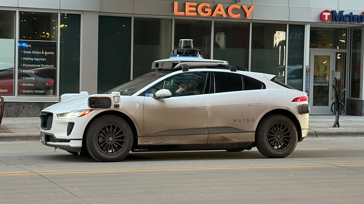 A white Waymo self-driving car with roof sensors on a street in downtown Minneapolis in February 2026