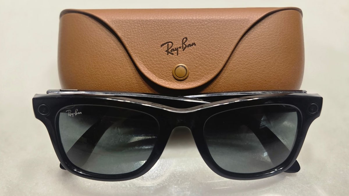 A pair of black Ray-Ban Meta smart glasses, with small camera openings at the corners of the frame, resting in front of a brown leather case