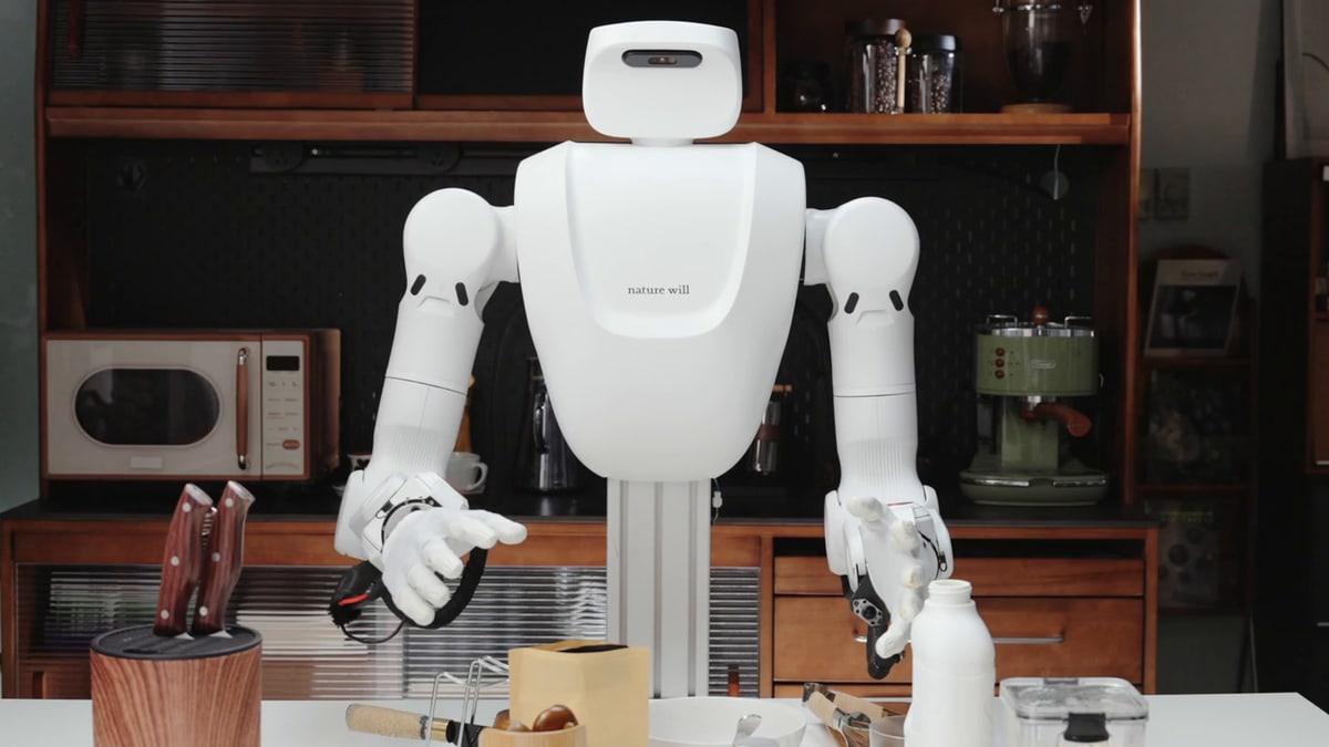 A white two-armed robot with Nature Will's name on its body and black-and-white robot hands, standing at a kitchen counter