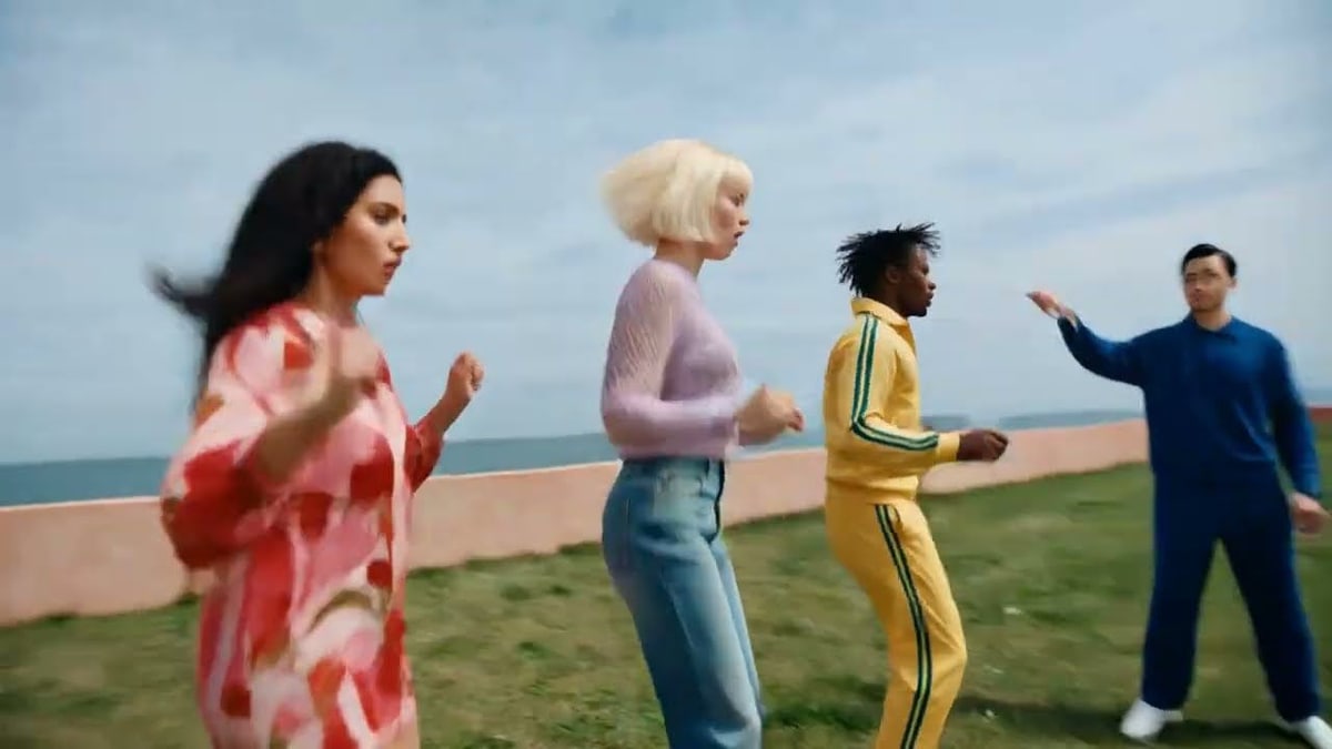 Four dancers in bright, mismatched outfits step in time across a lawn above the sea, from Pika's launch video