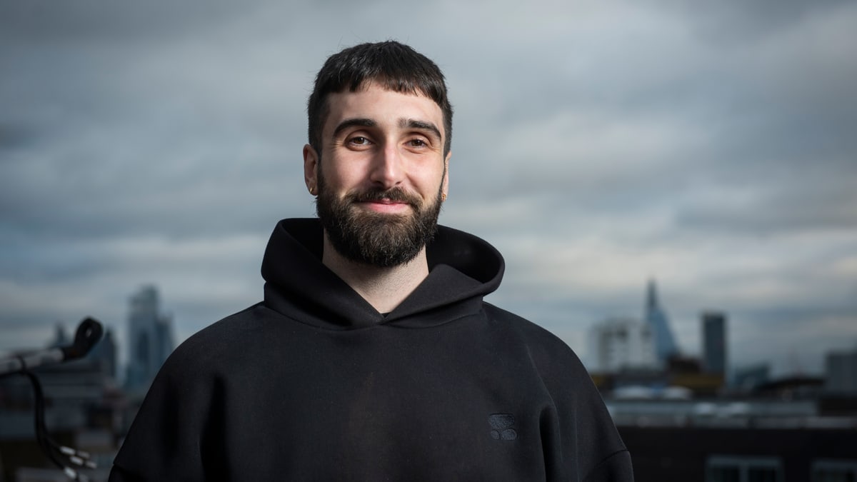 Cohere co-founder and chief executive Aidan Gomez, in a black hoodie, standing on a rooftop with a city skyline behind him