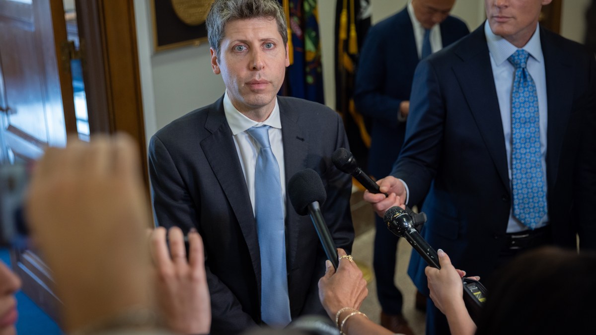 OpenAI chief executive Sam Altman speaking to reporters amid a cluster of microphones