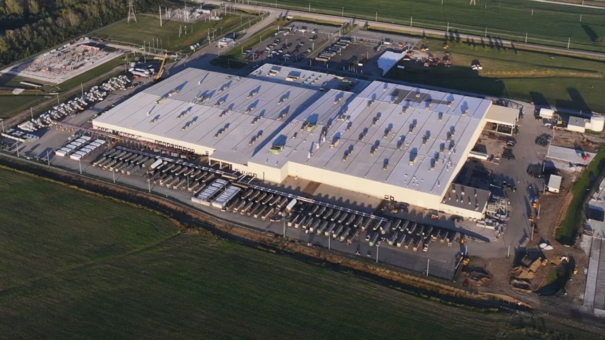 Aerial view of SpaceX's Colossus AI data center, a long white building surrounded by rows of equipment and fields