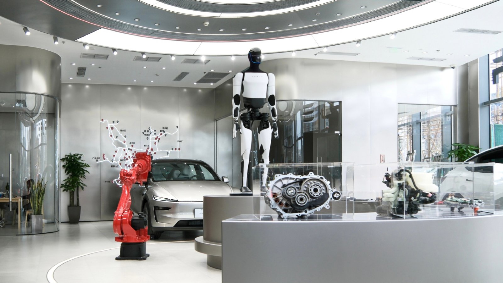 A Tesla Optimus humanoid robot on display at a Tesla store in Beijing beside a Model Y and drivetrain exhibits